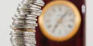 Coins Stacked on a Table with a Wallclock in the Background