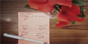 A piece of paper containing welcome messages placed on a table besides a flower vase